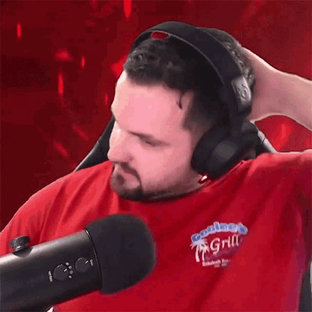 a man wearing headphones is sitting in front of a microphone and scratching his head .