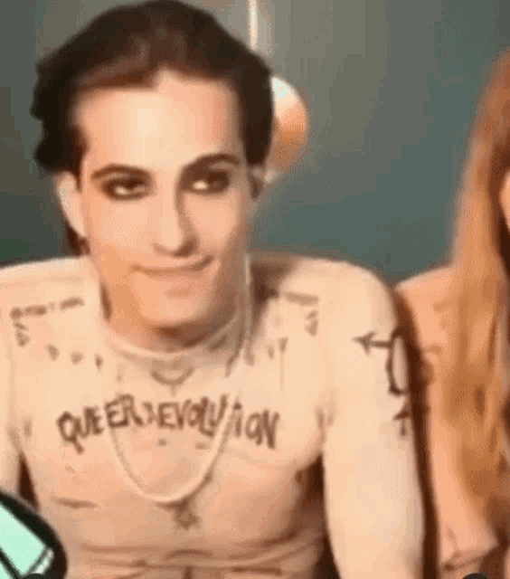 a man with a tattoo on his chest is smiling while wearing a necklace .