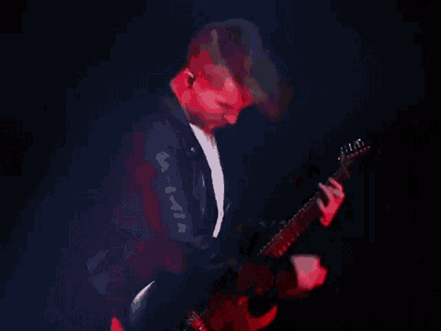 a man is playing a guitar in a dark room with red lights behind him .