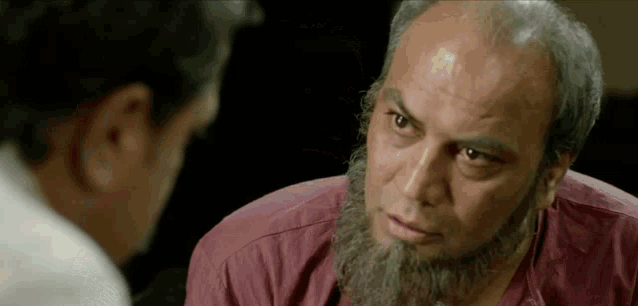 a bald man with a beard is talking to another man .