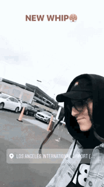 a man wearing a black hat and a hooded jacket is standing in a parking lot with the words new whip on the bottom