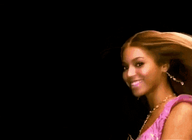 the woman is wearing a pink dress and a gold necklace and her hair is blowing in the wind .