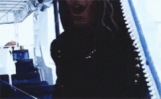 a woman in a black sweater is standing in a dark room with a blue railing