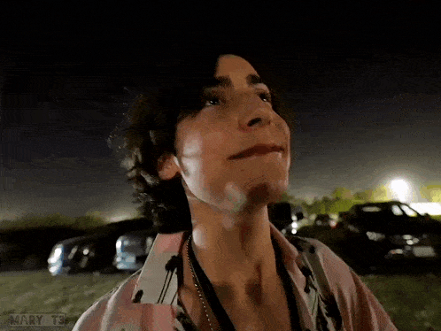 a man in a pink shirt is standing in a parking lot at night and says good night family