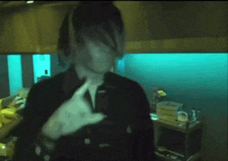 a man with long hair and dreadlocks is standing in a dark room with a blue light behind him .