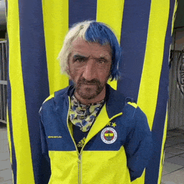 a man with blue hair and a beard wears a yellow adidas jacket