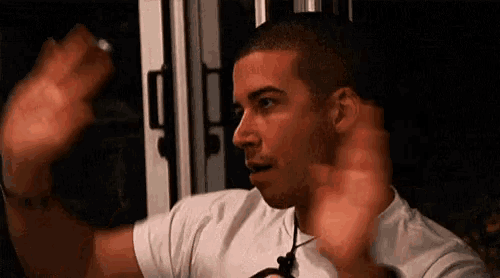 a man in a white shirt is standing in a dark room with his hands up .