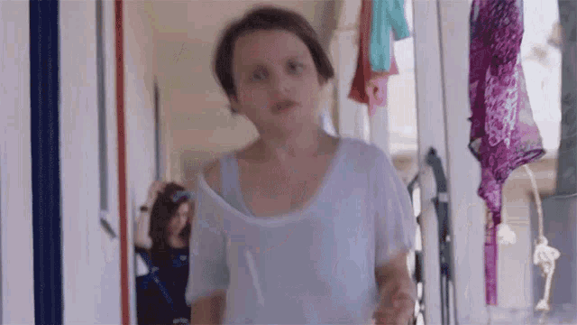 a girl in a white shirt is walking down a hallway with clothes hanging on the wall behind her .