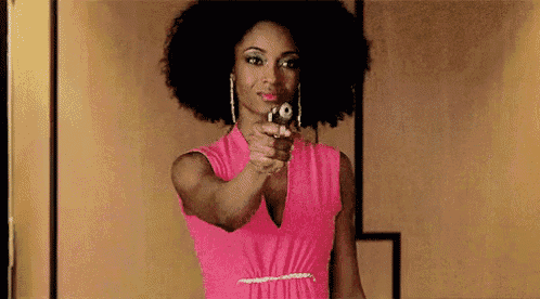 a woman in a pink dress is pointing a gun at the camera while standing in front of a mirror .