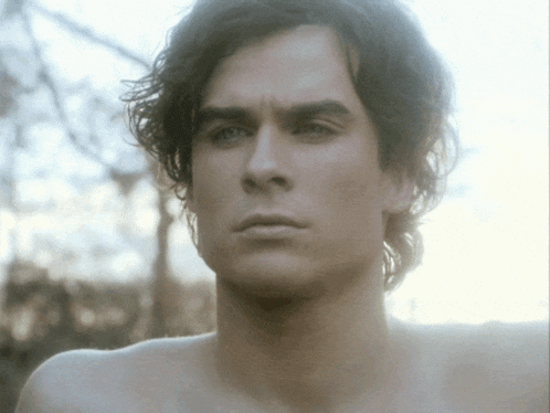 a close up of a shirtless man 's face with trees in the background