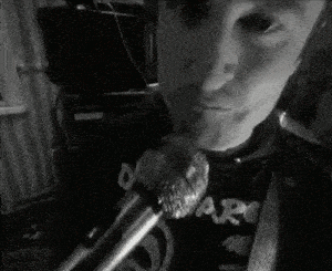 a man is singing into a microphone while wearing a shirt that says hard .