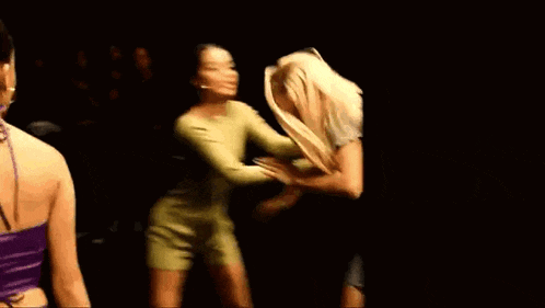 two women are standing next to each other in a dark room and fighting .