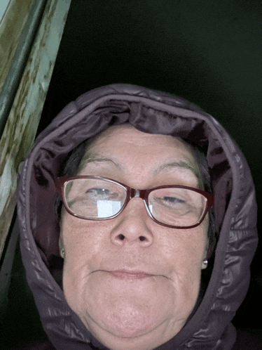 a woman wearing glasses and a hooded jacket is making a funny face