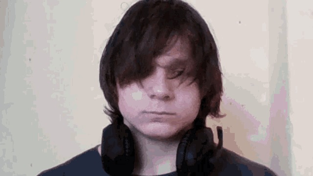 a young man with long hair is wearing headphones around his neck and making a funny face .