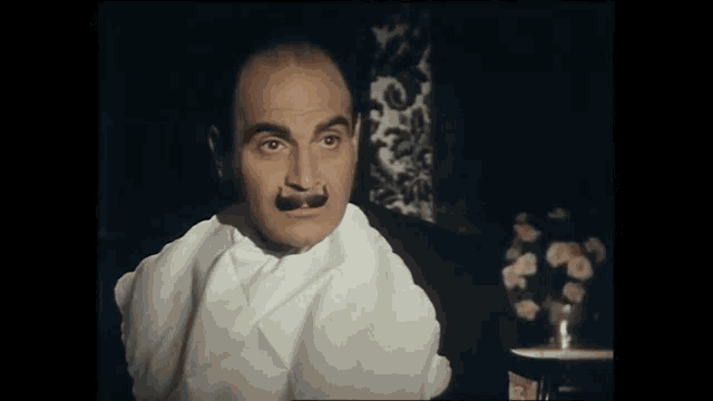 a man with a mustache and a white shirt looks at the camera
