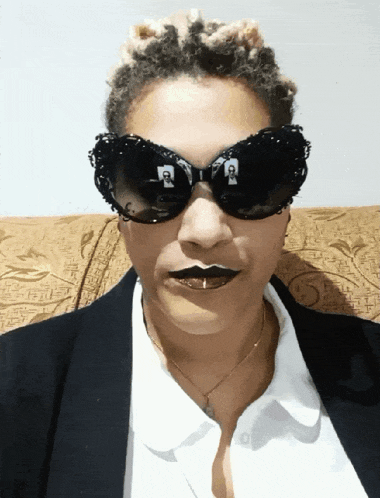 a woman wearing sunglasses has a reflection of a man in the lens