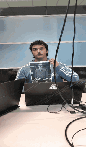 a man sitting at a desk holding a picture of a man named php lore