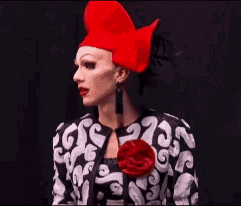 a drag queen is wearing a red hat and earrings .