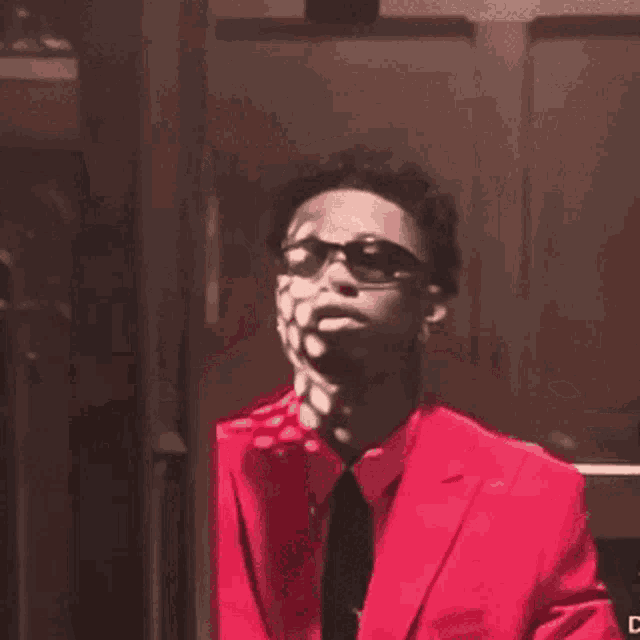 a man in a red suit and tie is wearing sunglasses and holding his hand to his chin .