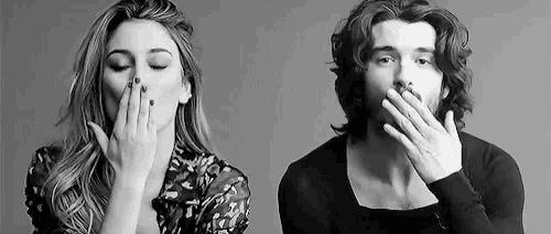 a black and white photo of a woman blowing a kiss and a man covering his mouth .