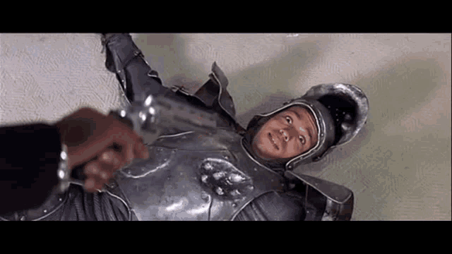 a man in armor is laying on the floor and a man is holding a knife .