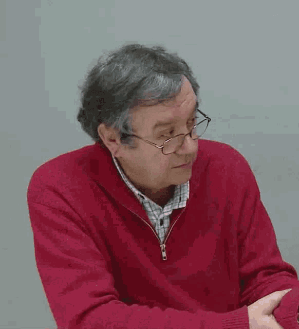 an older man wearing glasses and a red sweater