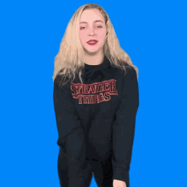 a girl wearing a stranger things sweatshirt stands in front of a blue background that says mange moi la moule
