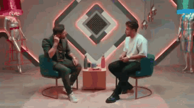 two men are sitting in chairs talking to each other in a room with mannequins in the background .