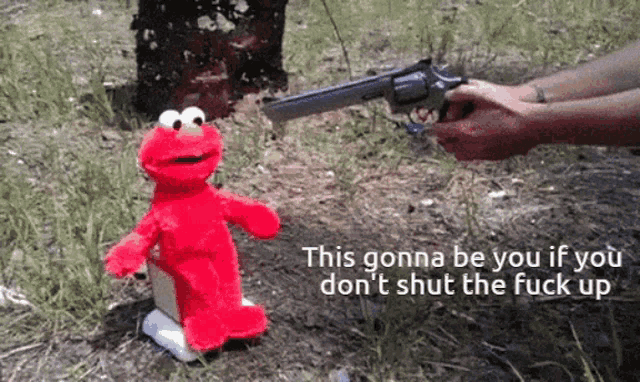 a person is holding a gun in front of a stuffed elmo