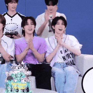 a group of young men are sitting on a couch with a cake in front of them and clapping .