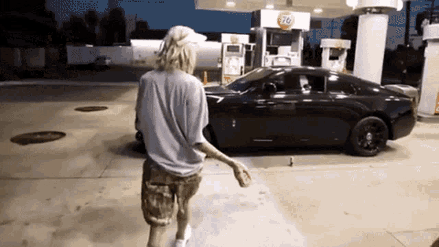a man is standing in front of a black car at a gas station