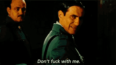 two men are standing next to each other in a dark room and one of them is saying `` don t fuck with me '' .