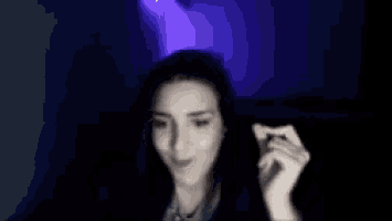 a blurry picture of a woman holding something in her hand in a dark room with purple lights .
