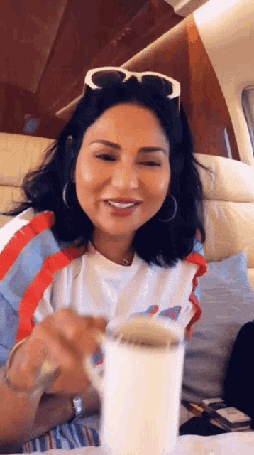 a woman wearing sunglasses sits at a table with a cup of coffee in her hand