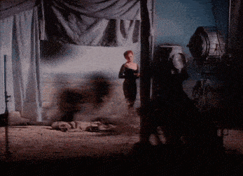 a woman in a black dress is standing in a dark room with a spotlight