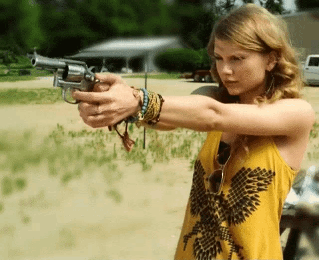 a woman in a yellow tank top holds a gun