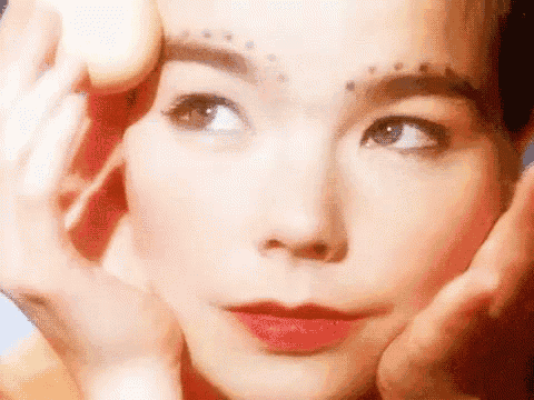 a close up of a woman 's face with her hands on her face and a tattoo on her forehead .