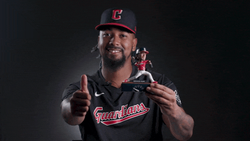 a man wearing a guardians jersey is holding a figurine and giving a thumbs up