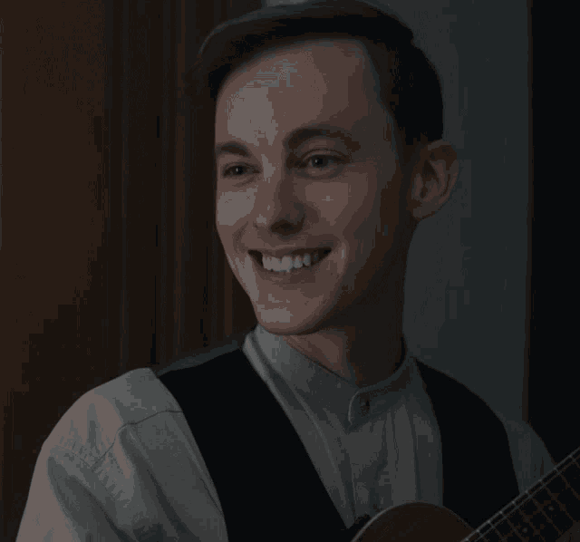 a man in a white shirt and black vest is smiling while holding a guitar