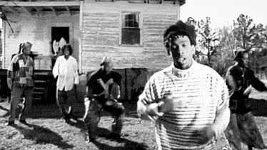 a black and white photo of a group of men dancing in front of a house .