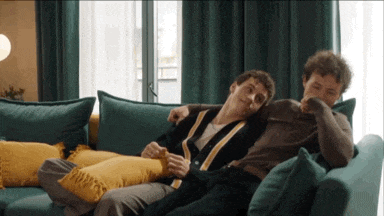 two men are laying on a blue couch and one has his arm around the other
