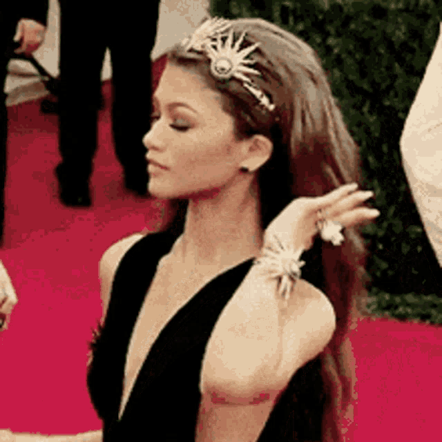 a woman in a black dress is standing on a red carpet with her hair in a headband .