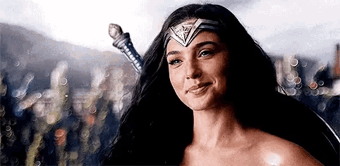 wonder woman is smiling while holding a sword in her hand .