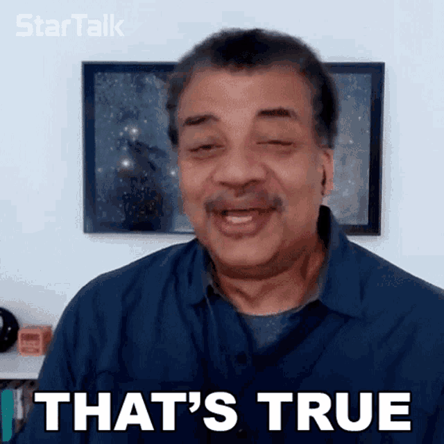 a man is smiling and saying that 's true in front of a framed picture .