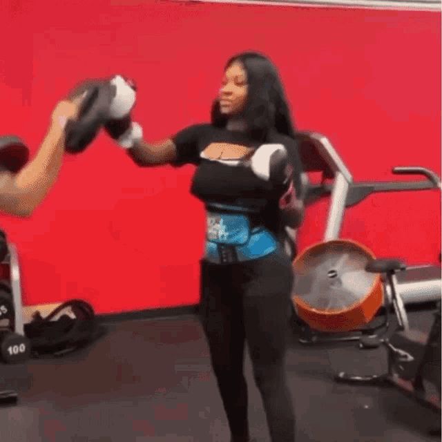 a woman wearing boxing gloves is standing in a gym