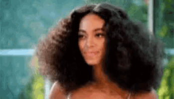 a woman with very large curly hair is smiling and looking at the camera .