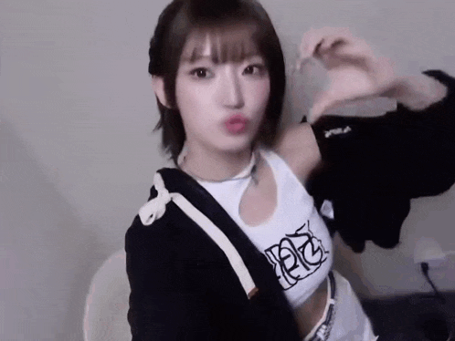 a young girl is making a heart shape with her hands while wearing a crop top and a black jacket .