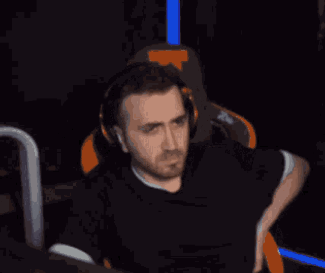 a man with a beard is sitting in a gaming chair with headphones on and a fist in his hand .