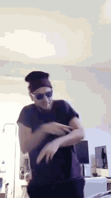 a man wearing sunglasses and a beanie is dancing in a living room .