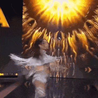a woman in a white dress is dancing on a stage in front of a huge screen .